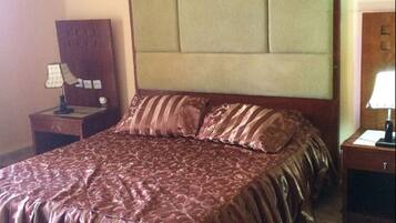 Une chambre d’hôtel avec un grand lit, une table de chevet, une lampe et une commode.