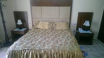 A hotel room with a large bed, two bedside tables with lamps, a wooden headboard, and a floral bedspread.