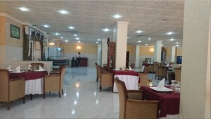 Un'ampia sala da pranzo con diversi tavoli e sedie, un pavimento in marmo lucido e un soffitto alto con illuminazione a incasso.
