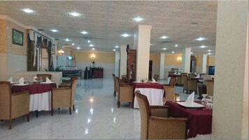 A spacious dining area with multiple tables and chairs, a polished marble floor, and a high ceiling with recessed lighting.