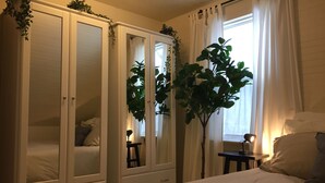 Un dormitorio con cama, armario, mesita de noche y ventana con cortinas.