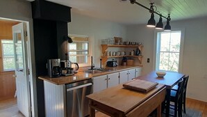 Una cocina compacta con lavavajillas integrado, encimeras de madera y una isla central con banco. Hay luces colgantes sobre la isla y un ventanal que proporciona luz natural.