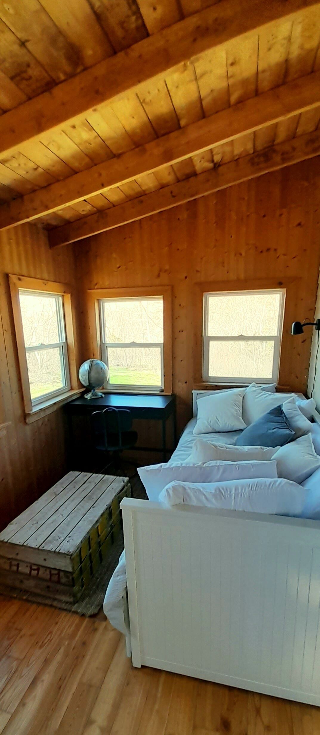 Habitació d'una cabana de fusta, amb un llit, dues finestres, un escriptori i una taula petita.