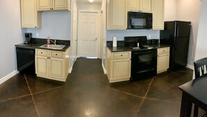 Una cocina con piso de baldosas oscuras, gabinetes de color crema, estufa negra, microondas y refrigerador.