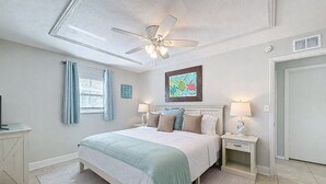 A bedroom with a bed, bedside tables, a ceiling fan, a window with curtains, and a wall-mounted artwork. - Coastal Escape Awaits: Enjoy a Complimentary Pontoon Boat Adventure! (New Port Richey)