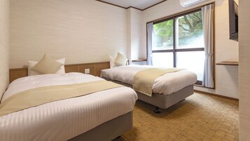 Habitación de hotel con dos camas, un ventanal grande y piso de madera.