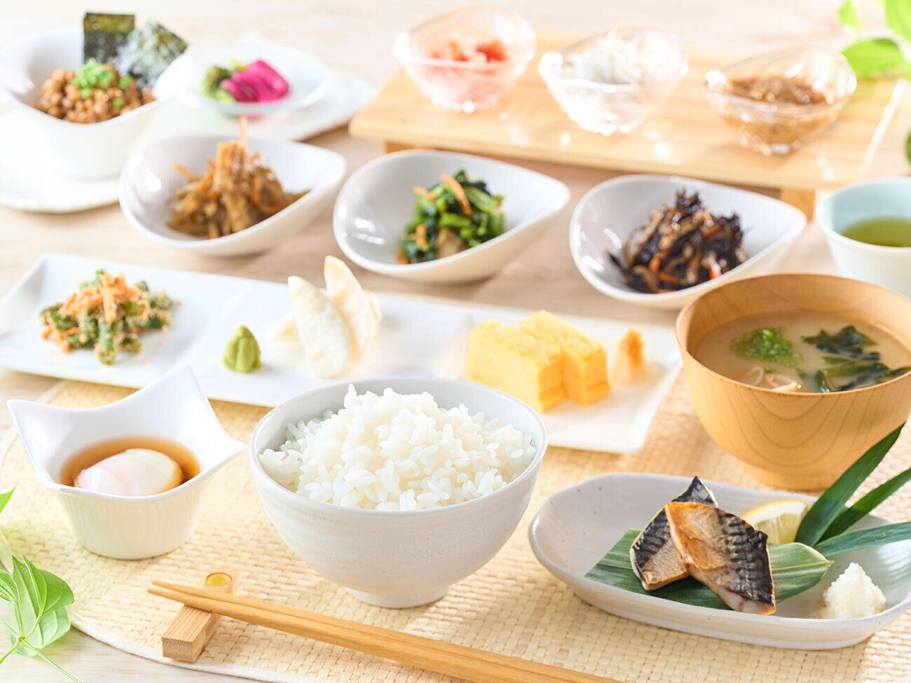 A variety of Japanese dishes including rice, fish, and vegetables, arranged on a table with chopsticks and bowls.