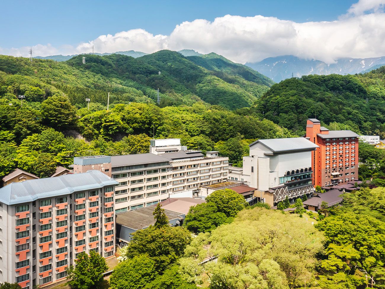 A multi-story building with a flat roof, surrounded by lush green trees and hills in the background.