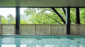 A covered swimming pool with a view of lush greenery and trees.