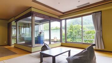 Una habitación con un gran ventanal corredera que da a un balcón, una mesa pequeña con sillas y vistas al exterior con vegetación.