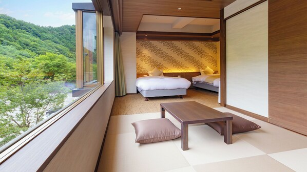Una habitación con un ventanal grande, una cama, una mesita de noche y vistas a un área boscosa.