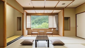 A traditional Japanese room with tatami flooring, a low table, two chairs, and a view of a forest through shoji screens. - Ooedo Onsen Monogatari Premium Matsunoi (Minakami)