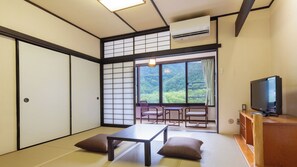 Une pièce de style japonais traditionnel, avec un sol recouvert de tatamis, une table basse, des coussins, un téléviseur et une porte coulissante.