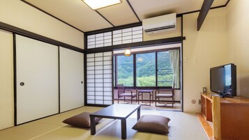 Una habitación japonesa tradicional con suelo de tatami, una mesa baja, cojines, un televisor y un puertas correderas.