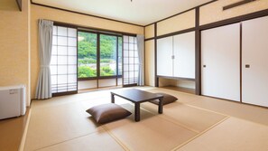Et traditionelt japansk rum med tatami-gulv, et lavt bord, puder, skydedøre og udsigt til grønne områder.