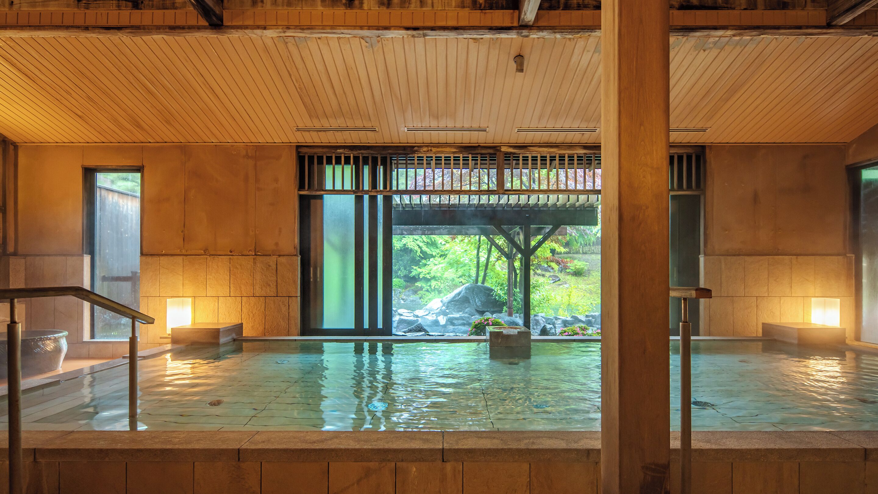 A wooden interior with a large window, a stone basin, and a wooden structure outside.