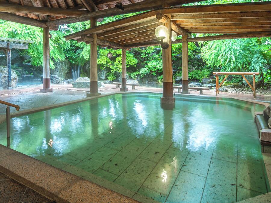 Una estructura de madera con piscina, escalones de piedra y una escultura de piedra.