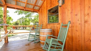 A wooden cabin with a porch, two rocking chairs, a barrel, and a window. - God's Country Cabin- Faith I Country Retreat (Fredericksburg)