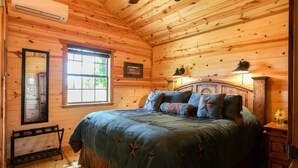 A wooden cabin bedroom with a bed, a window, a mirror, and a nightstand. - God's Country Cabin- Faith I Country Retreat (Fredericksburg)
