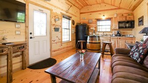 A cozy cabin interior with a wooden interior, a dining table, a sofa, a kitchen area, and a television. - God's Country Cabin- Faith I Country Retreat (Fredericksburg)