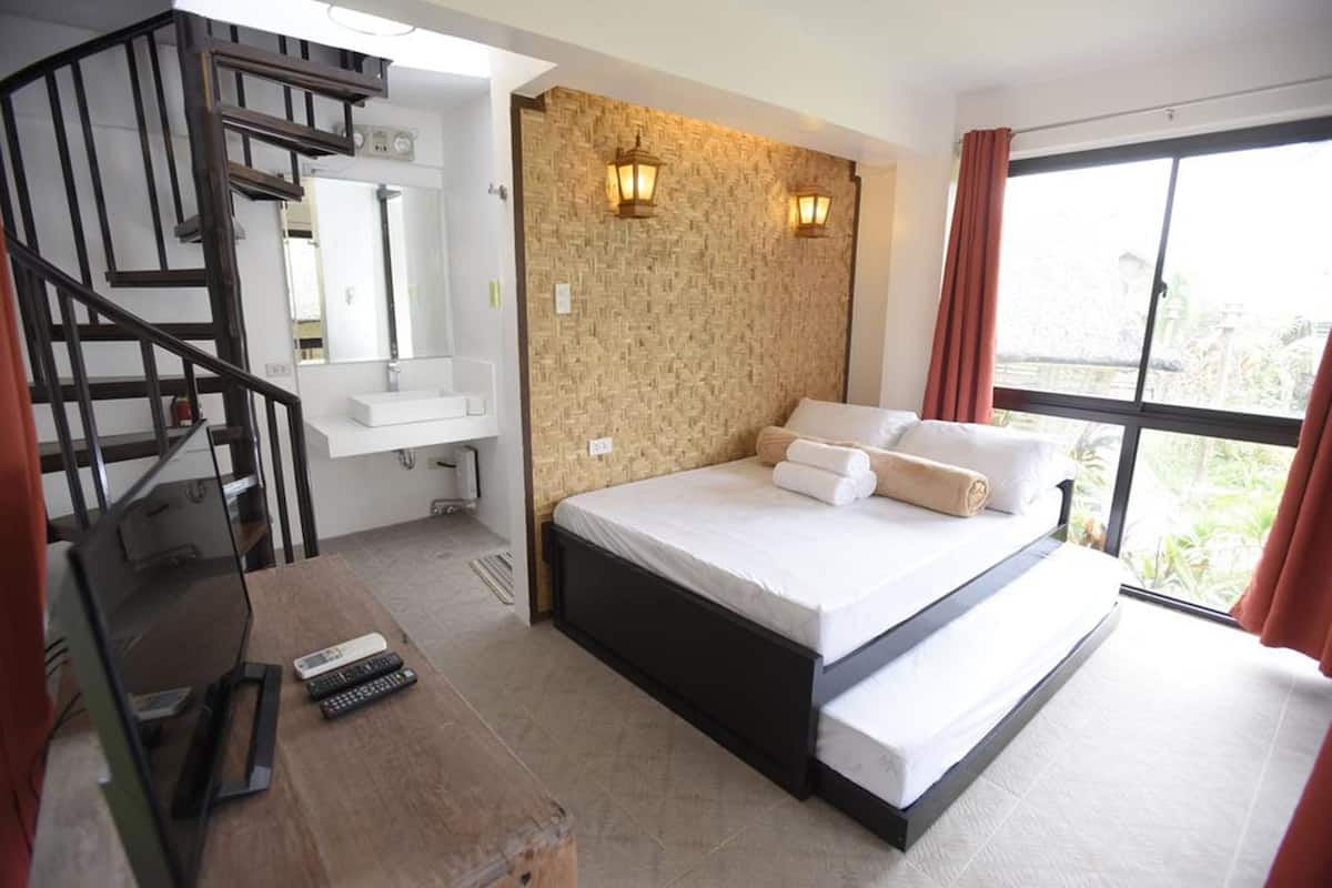 Un dormitorio con cama, un escritorio de madera, televisor, baño y ventana con cortinas.