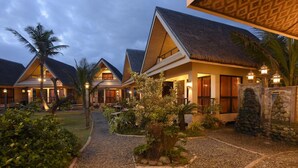 A resort with multiple bungalow-style buildings, each with a thatched roof and surrounded by landscaped gardens. - Nalu Surf Camp (Baler)