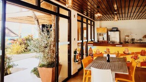 An indoor dining area with wooden ceiling, large windows, and a view of a tropical landscape. - Nalu Surf Camp (Baler)
