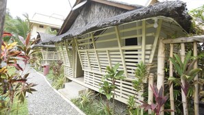 A traditional thatched-roof structure with a wooden lattice facade, surrounded by tropical plants. - Nalu Surf Camp (Baler)