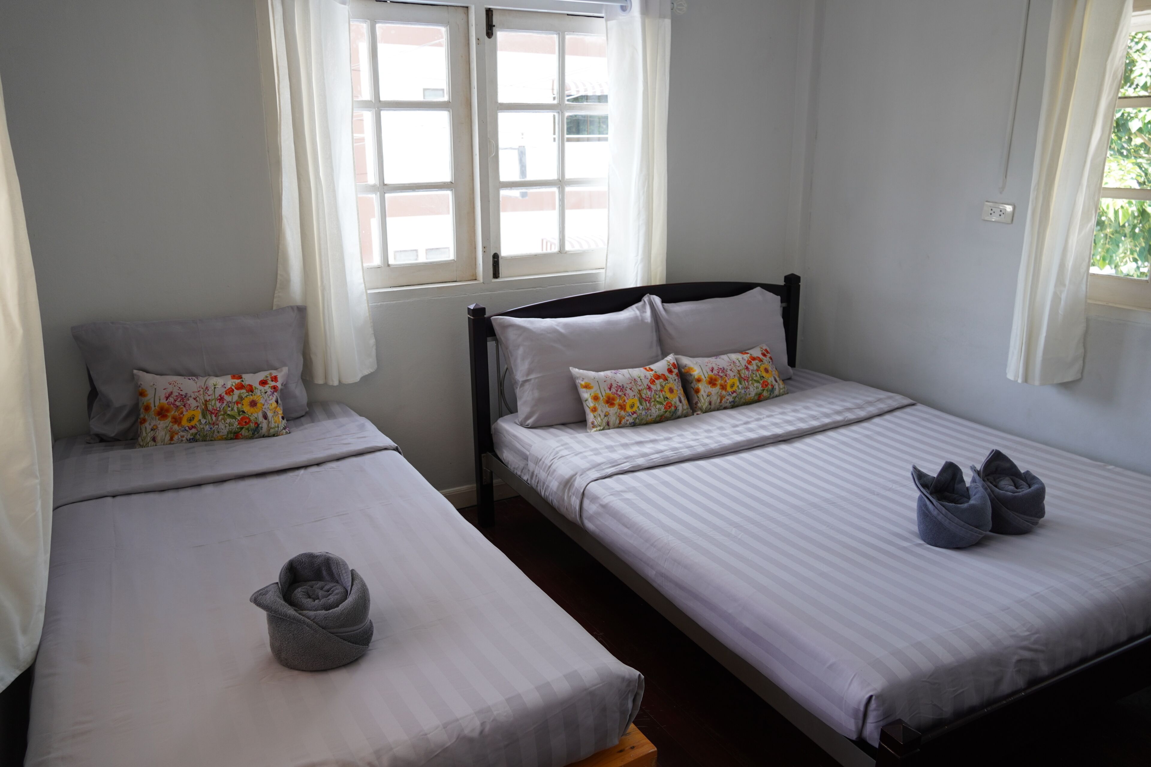 Two single beds with white bedding and floral pillows, a grey towel, and a pair of grey slippers on the right bed.