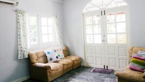 Een kamer met een beige leren bank, een witte deur en een raam met gordijnen.