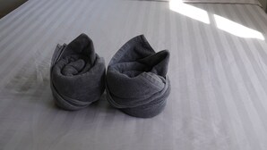Een bed met een gestreept dekbedovertrek, twee bloemenkussens en een paar grijze slippers op het bed.