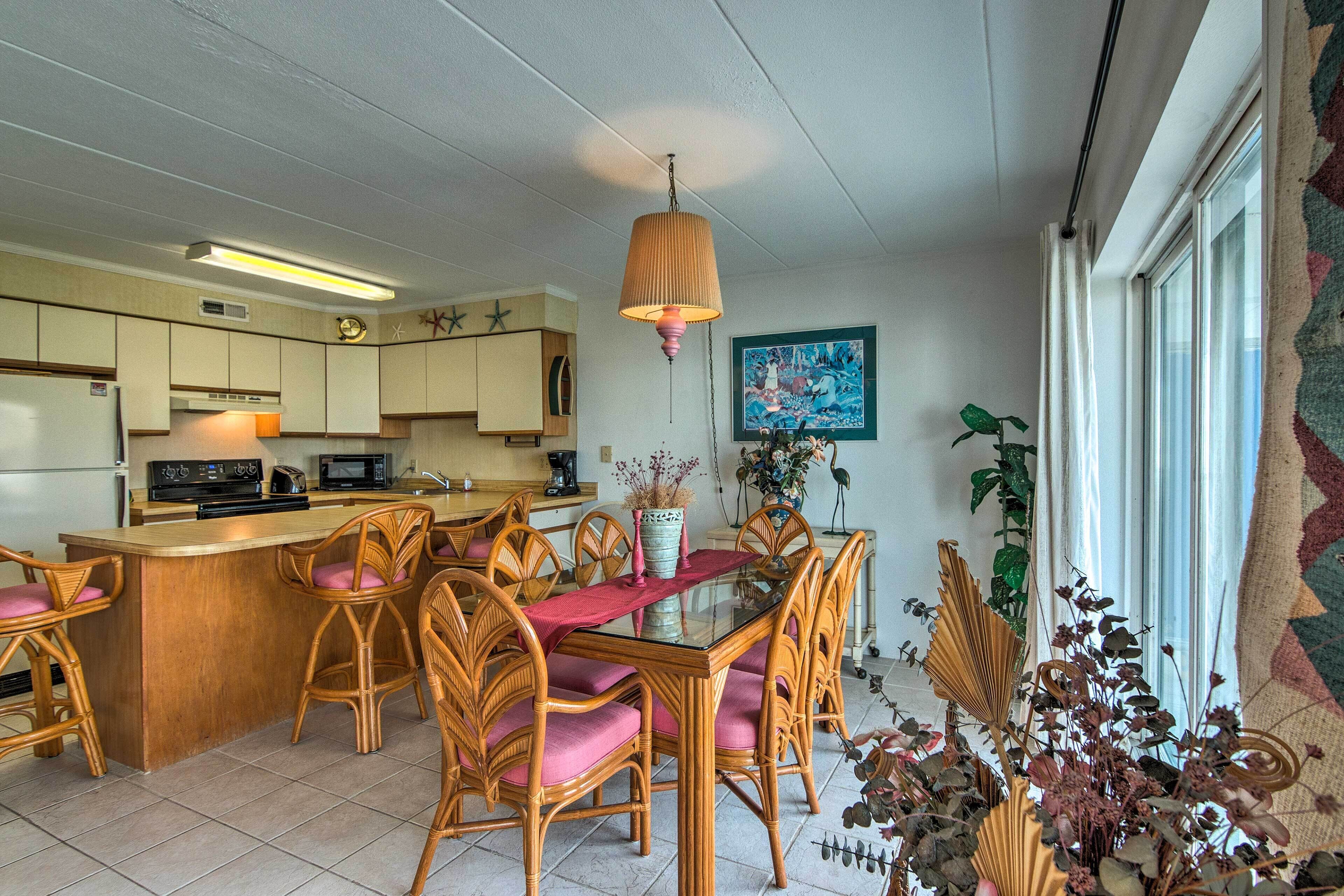 Une cuisine dotée d’un îlot central, de chaises en bois avec des coussins roses et d’une lampe suspendue.