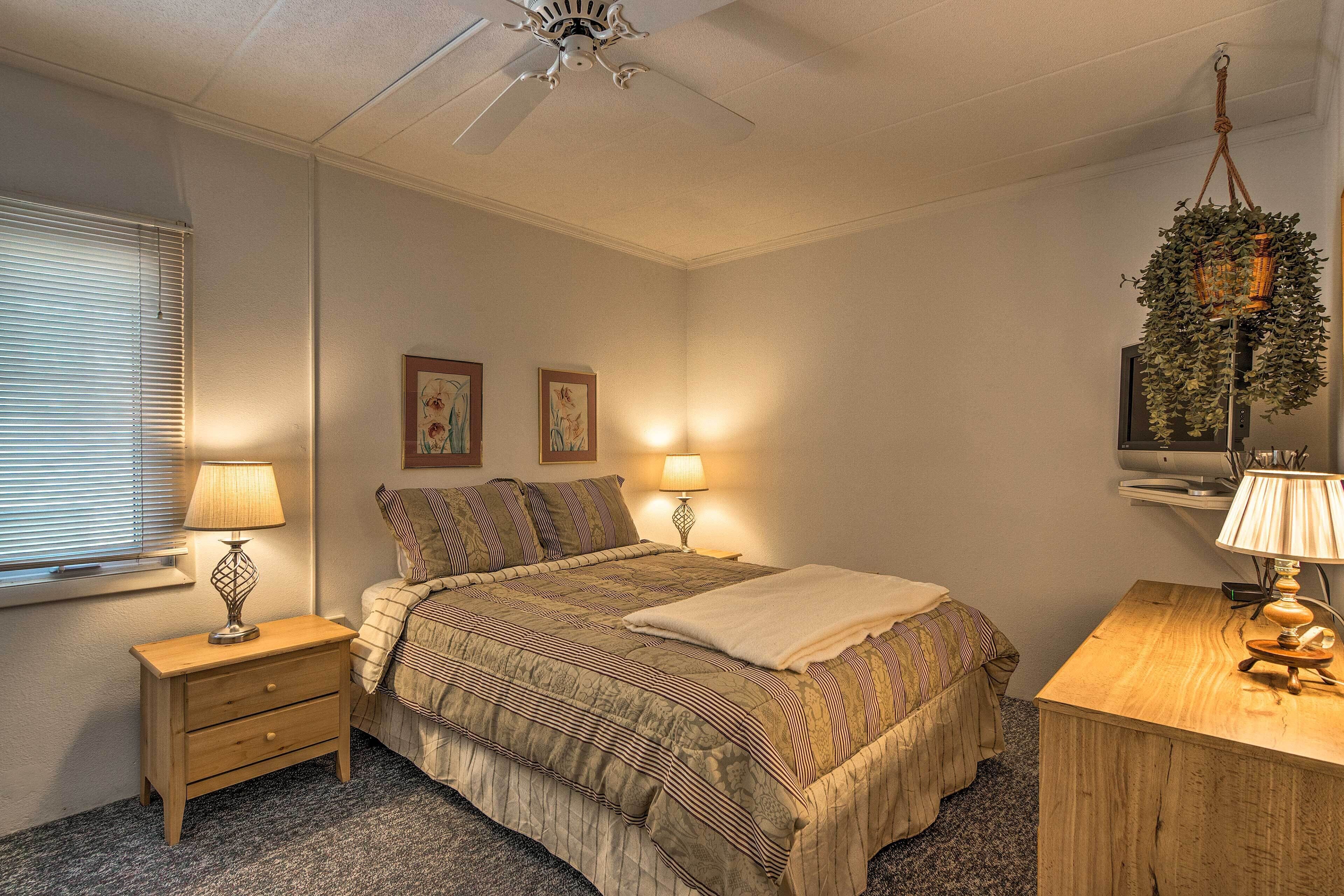A bedroom with a bed, bedside tables, lamps, a ceiling fan, and a hanging plant.