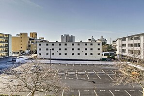 Un parcheggio con posti delimitati, un edificio bianco con diverse finestre e edifici residenziali circostanti.