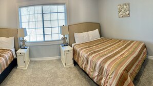 A bedroom with two beds, a window with blinds, a wall-mounted air conditioner, and a small decorative piece on the wall. - Watkins Glen 3-Bedroom Suites Unit 4 (Watkins Glen)