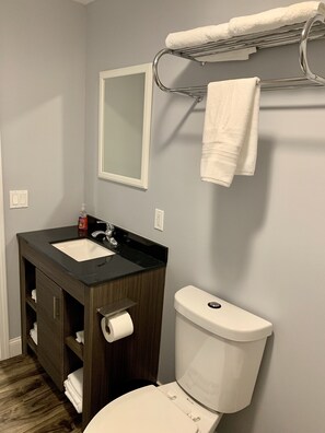Un baño con tocador de madera oscura, inodoro blanco y toallero sobre el lavamanos.