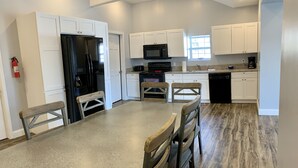 A modern kitchen with white cabinets, a black refrigerator, a microwave, and a dishwasher. There is a wooden dining table with chairs. - 405 S. Madison, Suite B (Watkins Glen)