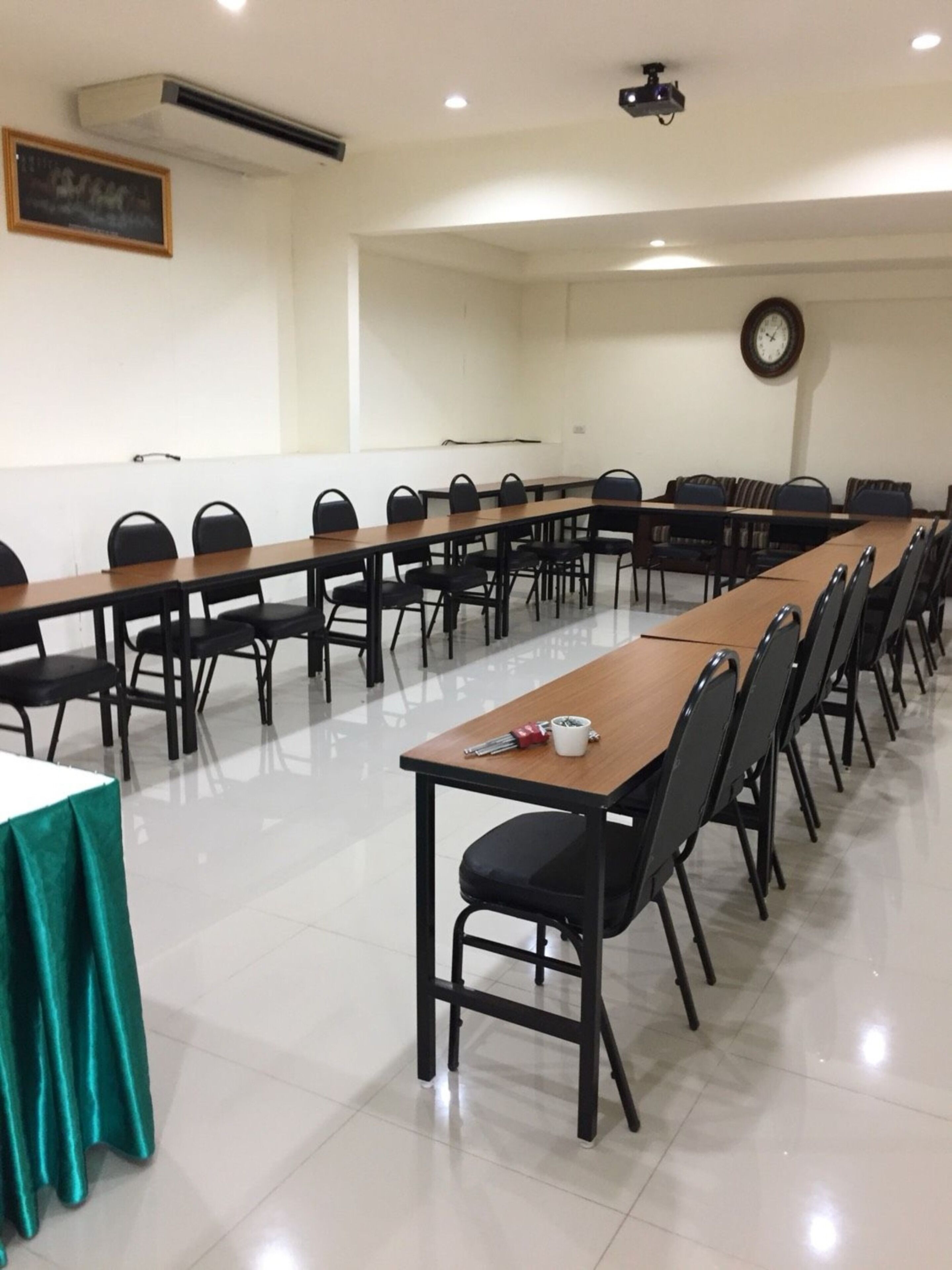 Una sala de conferencias con largas mesas y sillas, un reloj en la pared y un equipo de aire acondicionado.