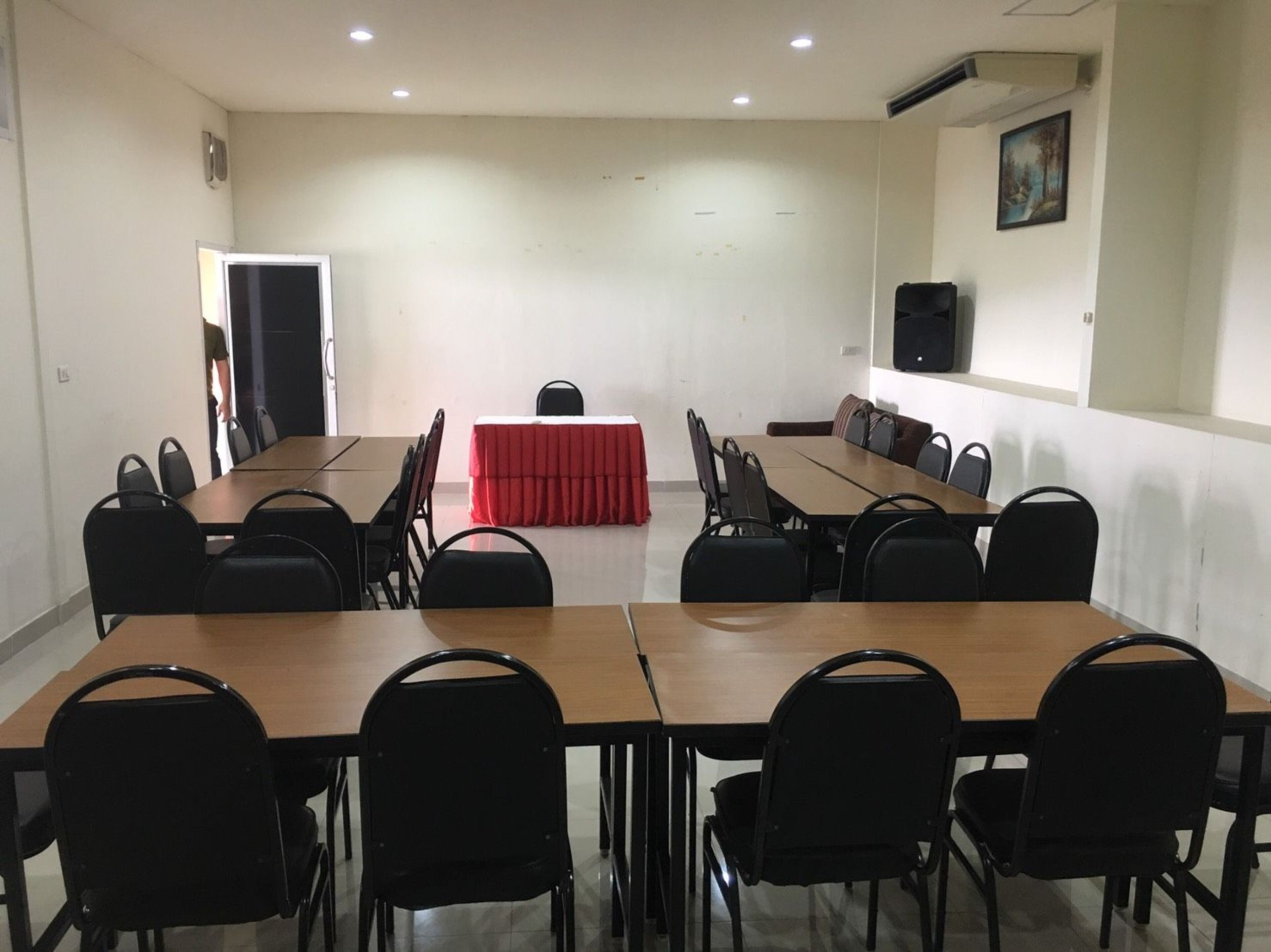 A conference room with a long table and chairs, a red tablecloth, and a speaker on the wall.