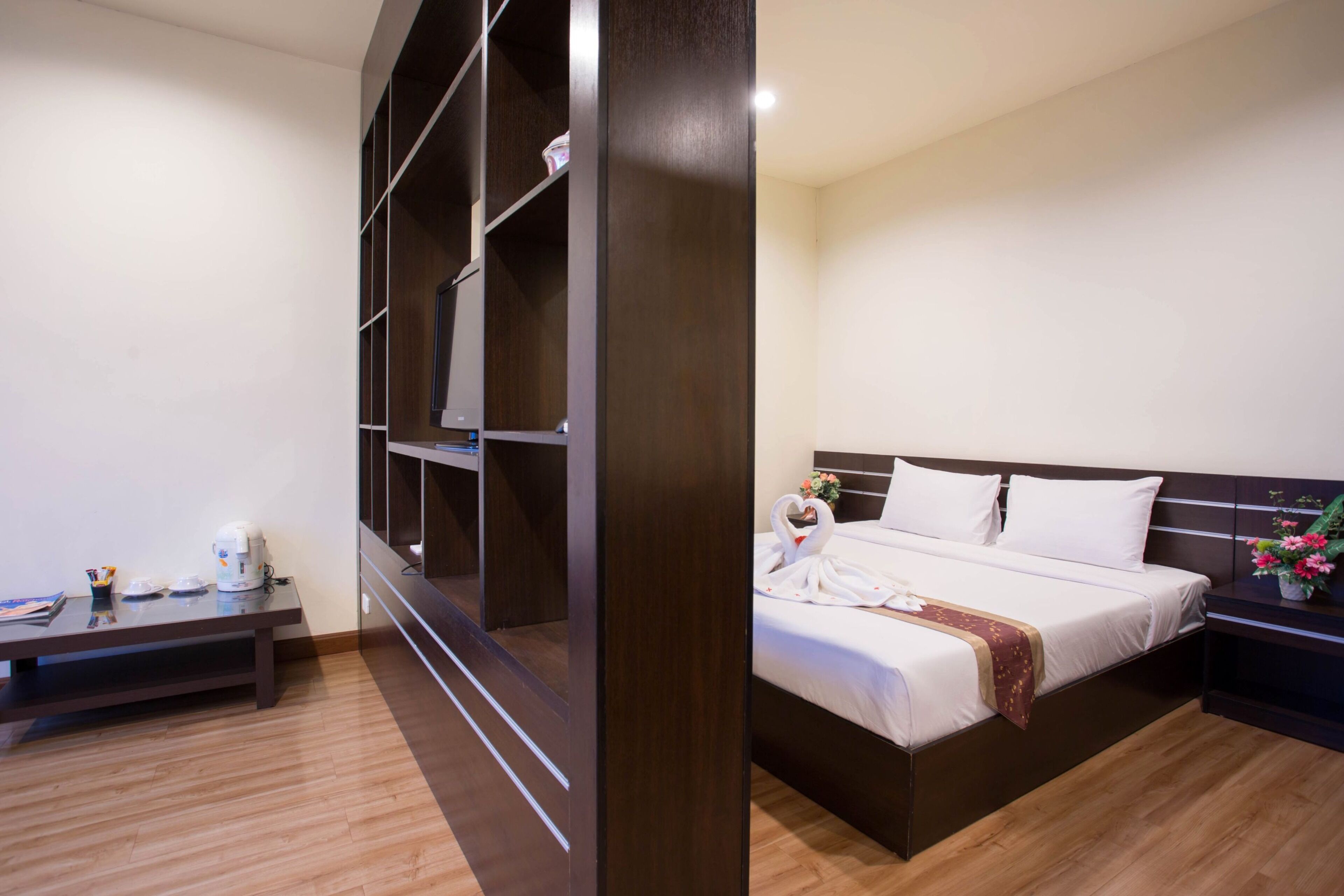 A hotel room with a bed, a nightstand, a wooden desk, and a built-in wardrobe.