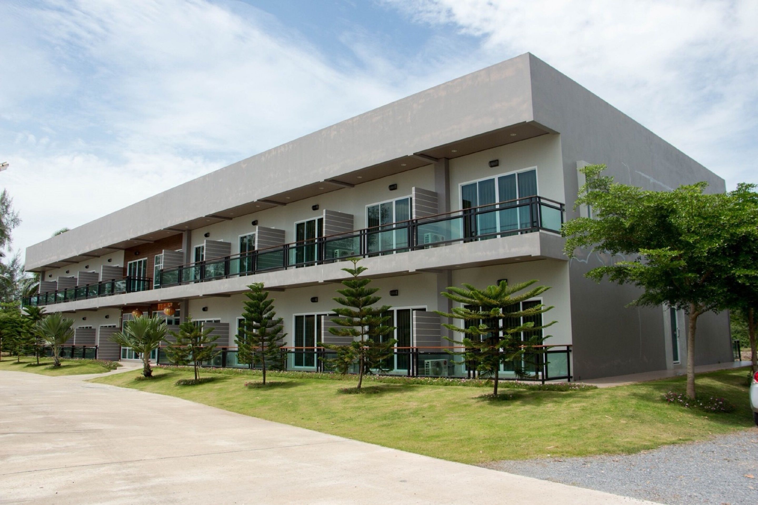 Um edifício moderno de vários andares com varandas, um caminho de paralelepípedos e pequenas árvores.