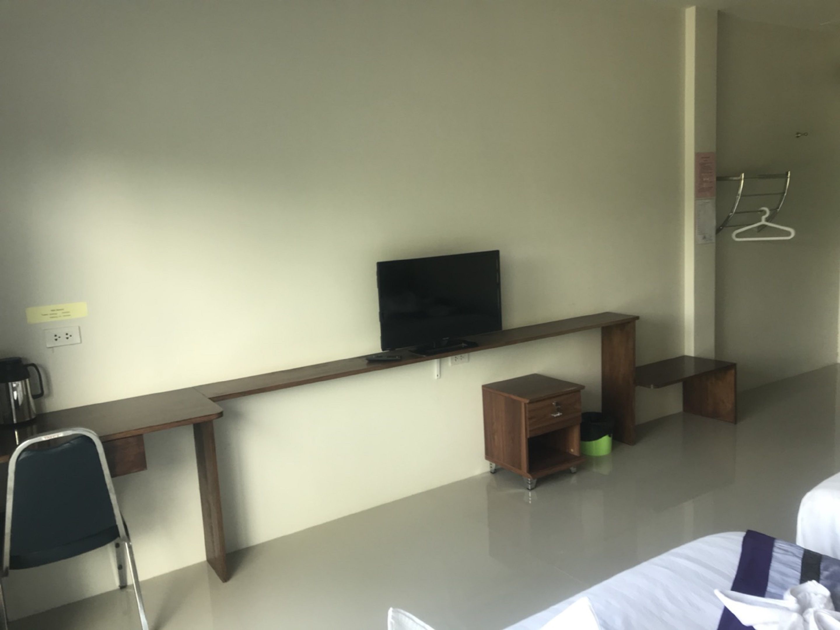 A hotel room with a bed, a desk with a television, a small cabinet, and a chair.