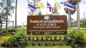 A sign for Haadthong Travel & Resort with multiple flags, surrounded by potted plants. - Hadthong Resort (Pak Phayun)