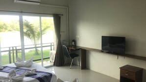 A hotel room with two beds, a TV, a desk, and a view of greenery outside. - Hadthong Resort (Pak Phayun)
