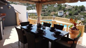 A dining table set for four with black plates and bowls, surrounded by wicker chairs, overlooking a pool and hillside homes. - Beautiful 3 bed,2 bath villa with private pool, views, a/c,wifi,new full kitchen (Alacant)