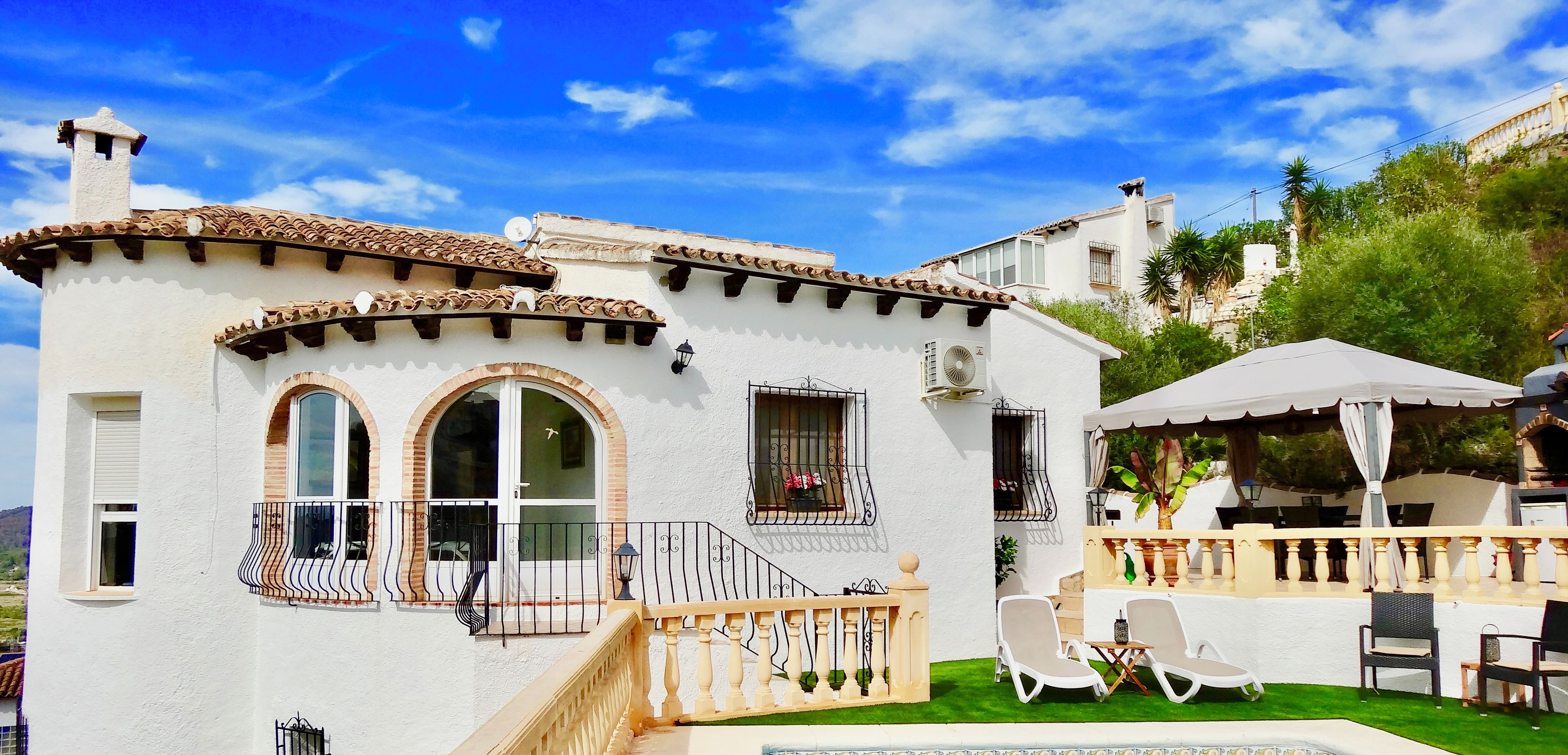 A white building with a tiled roof, a pool, and outdoor seating.