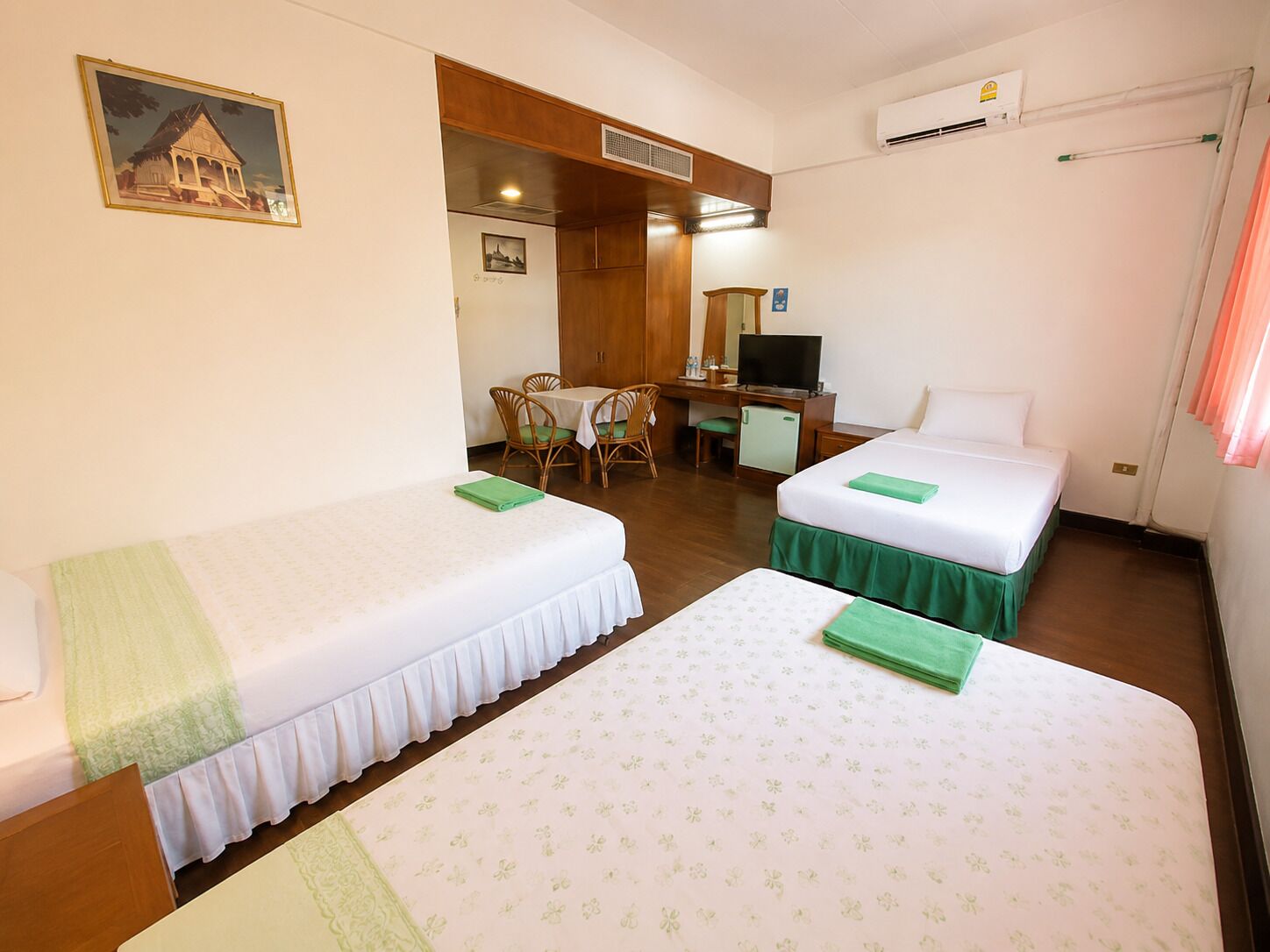 A hotel room with two beds, a desk, a chair, a television, and an air conditioning unit.