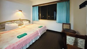 Una habitación de hotel con dos camas, una mesita de noche, una ventana con cortinas y una lámpara de pared.