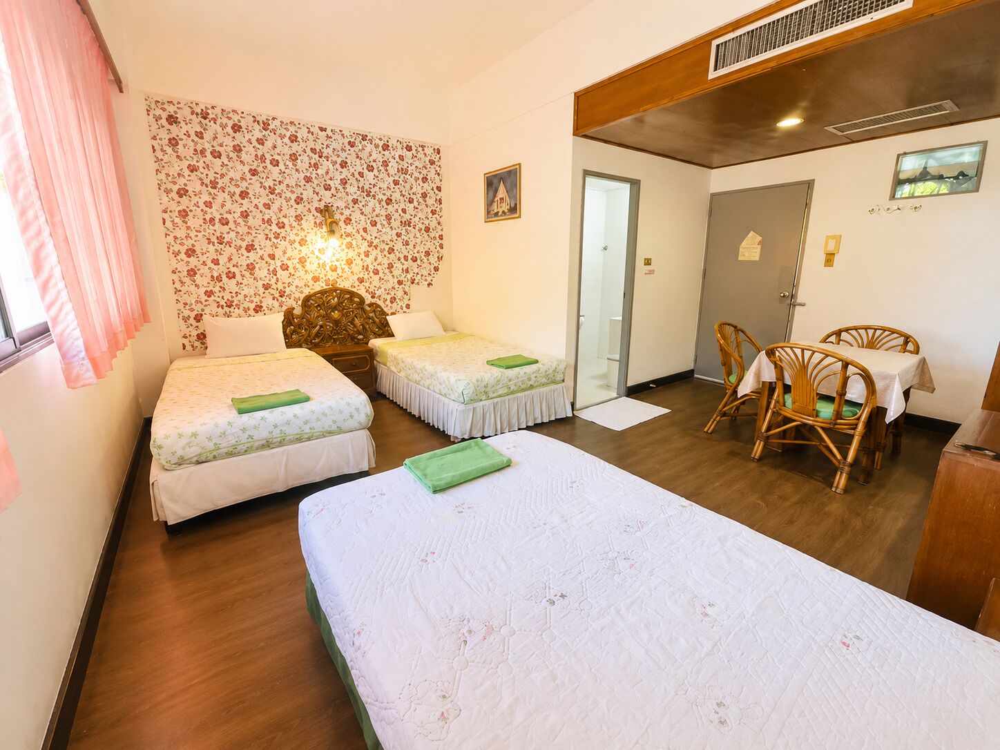 A room with two beds, a dining table with chairs, and a door leading to a bathroom.