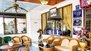 Una habitación con sofá, sillas, una mesa, ventilador de techo y ventana con cortinas.